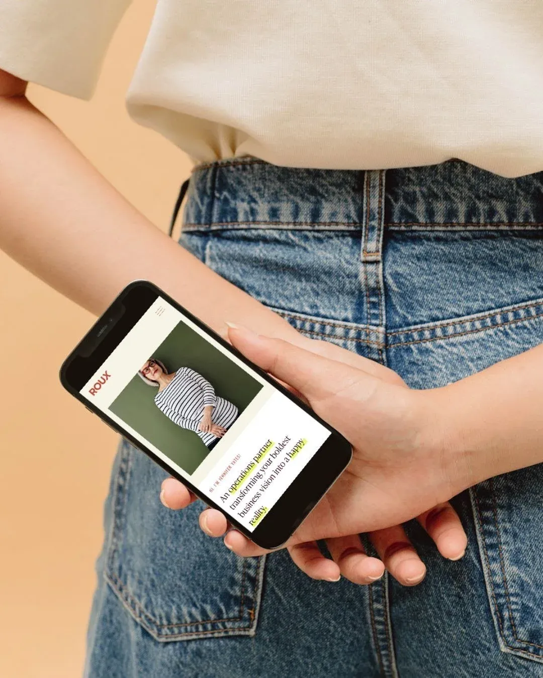 Hand holding a phone showing a website behind the back pocket of jeans