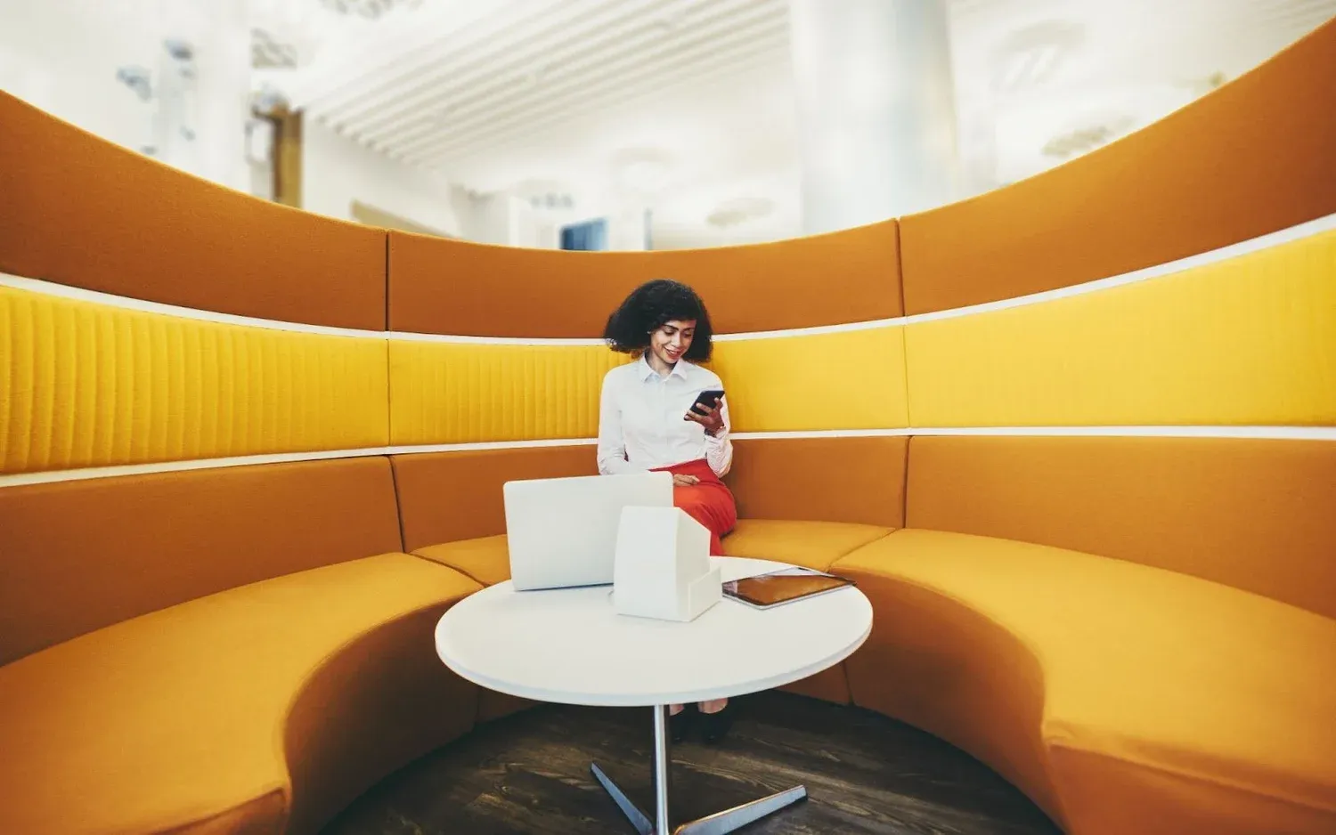 Woman on her phone in a curved mustard-yellow booth with a laptop