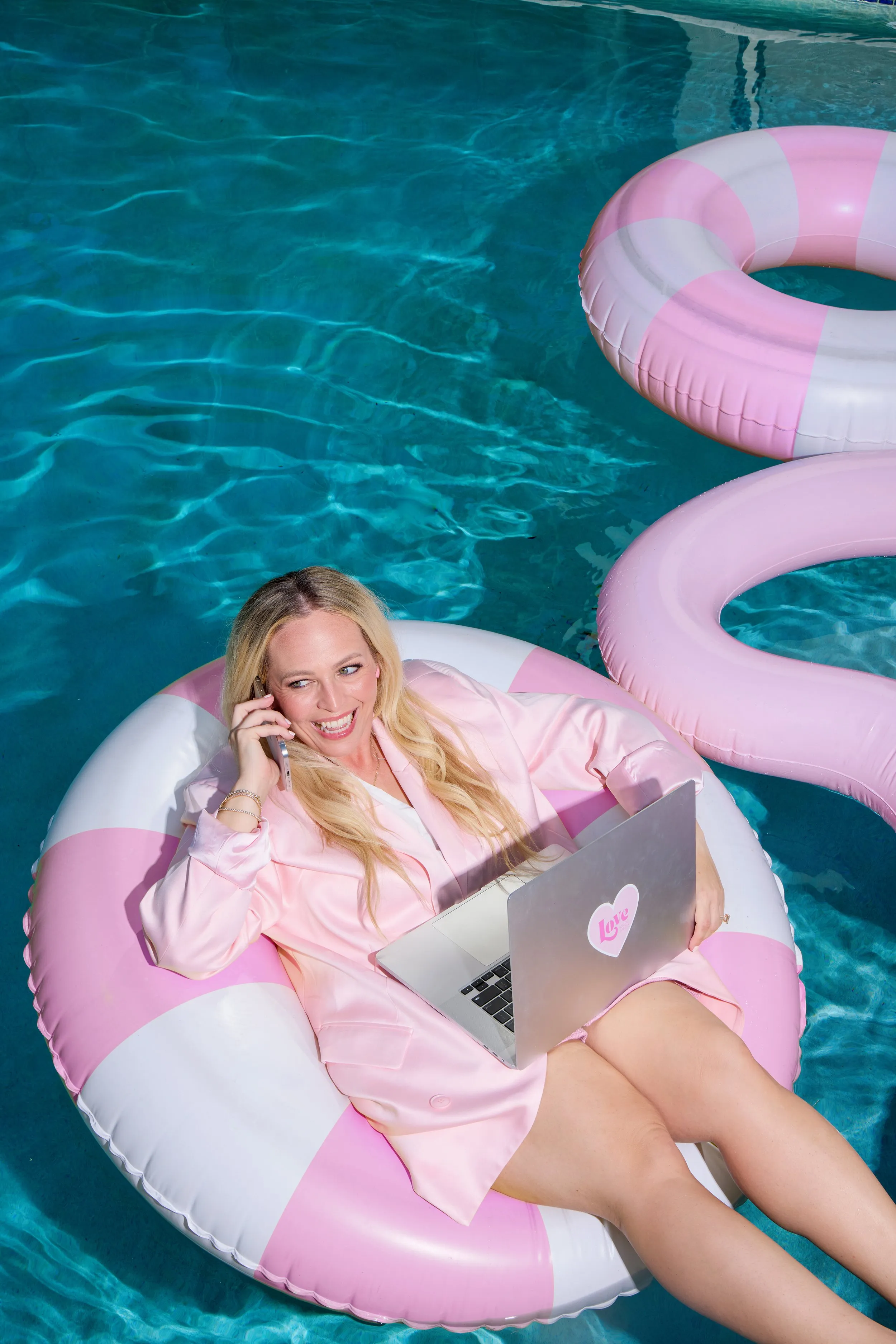 Woman relaxing on a pink and white pool float with a laptop