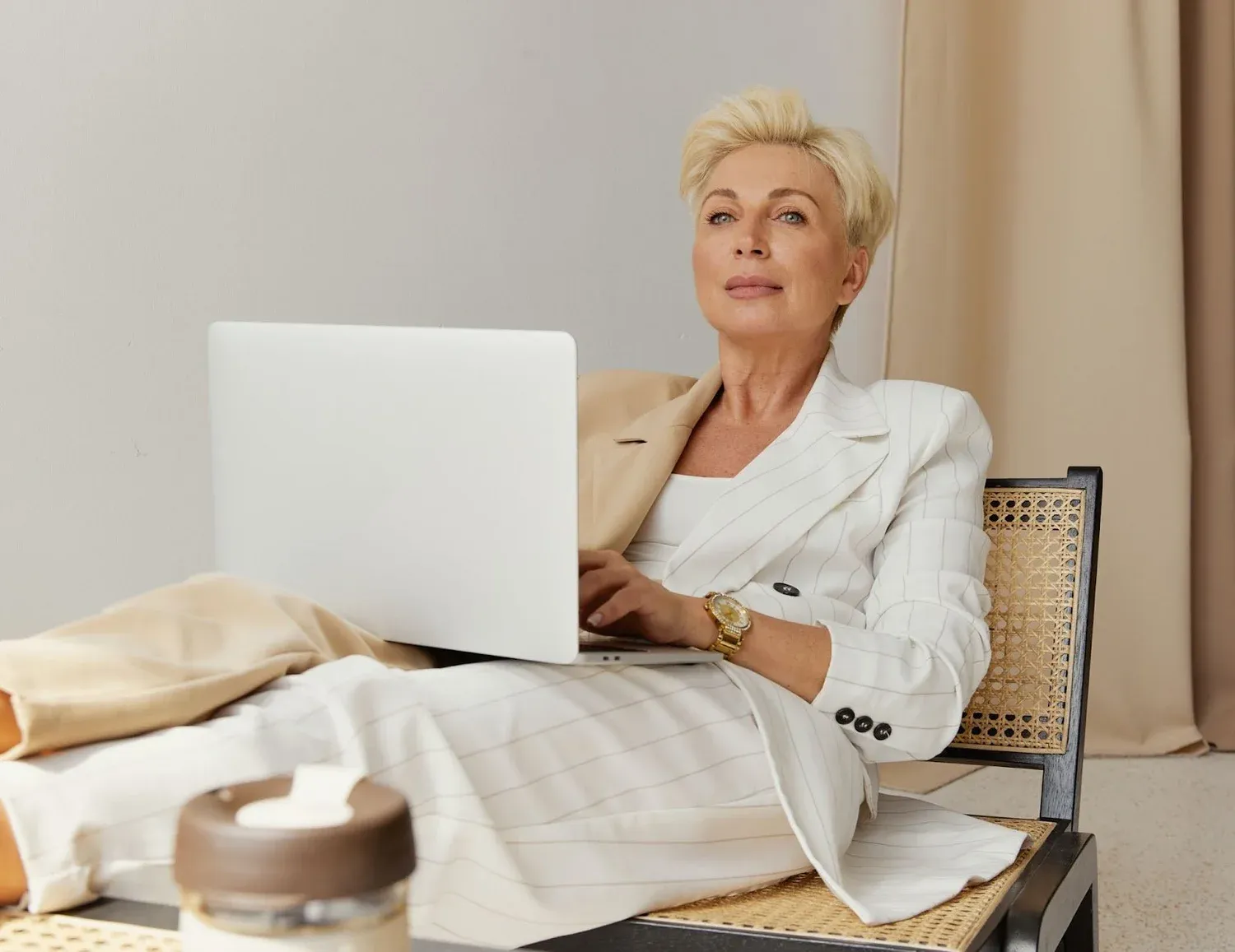 Woman in a white suit working on a laptop in a cane chair
